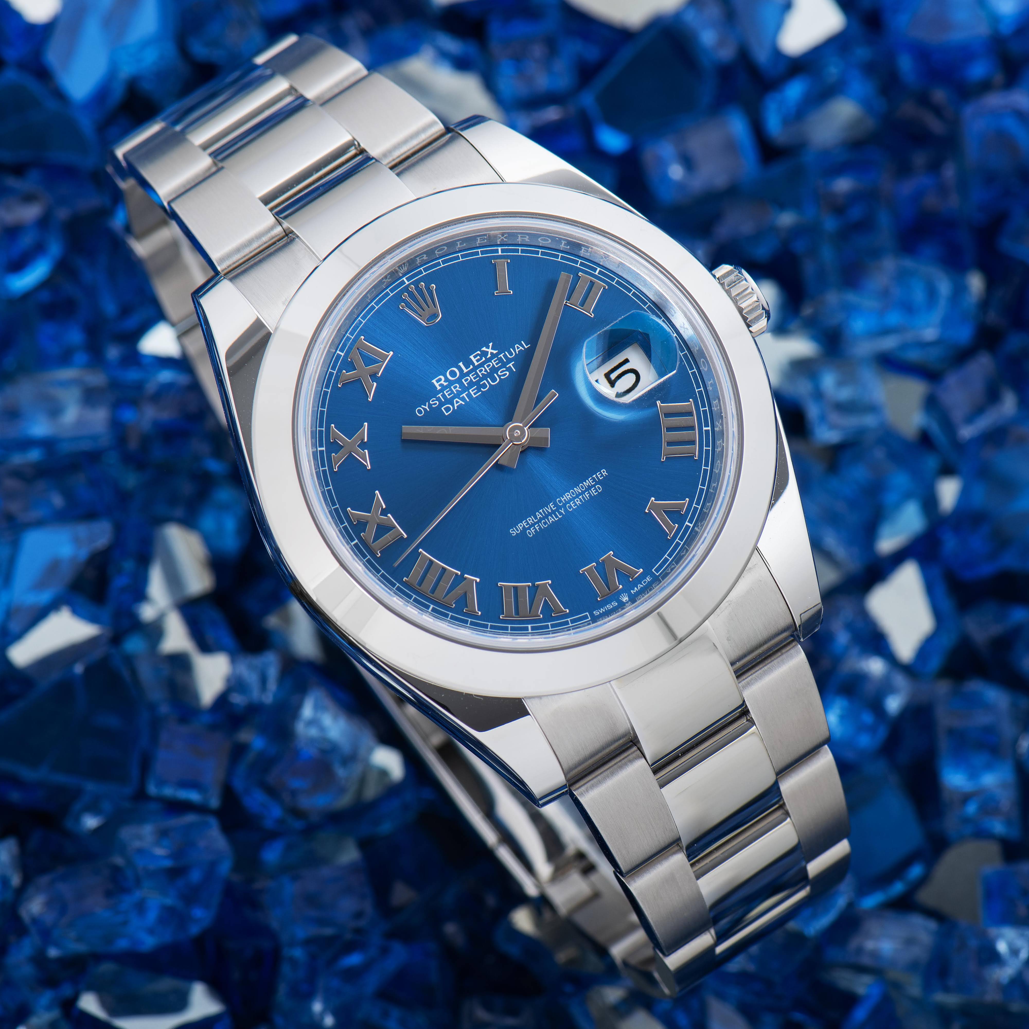 A genuine Rolex Datejust 41 with an azzurro blue Roman dial on an Oyster bracelet, shown dial-forward on a blue crushed-glass background