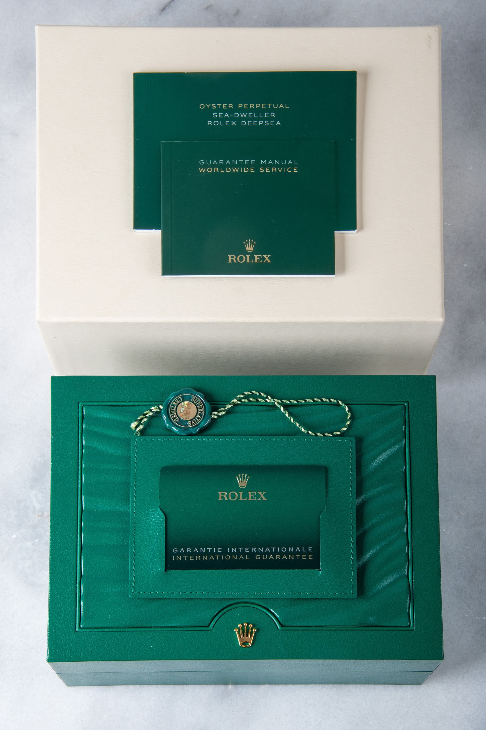 A Rolex Sea-Dweller shown with its original box, warranty card, and booklets — a full set — on a blue crushed-glass background